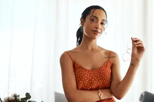 A woman wearing an orange polka-dot dress and holding a pair of glasses
