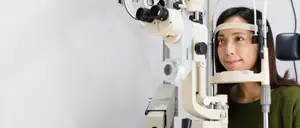 A woman wearing glasses is undergoing an eye examination using an ophthalmoscope.