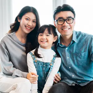 A family of three sitting together, smiling, and posing for a picture in a room with white walls and curtains.