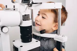 A child looks into a machine, possibly for an eye examination, smiling in a medical setting.