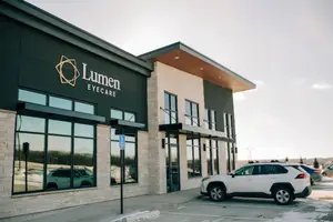 A white SUV is parked in front of the Lumen Eyecare building.