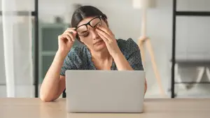 Stressed woman with glasses looking at a laptop while having a headache.