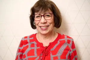 Portrait of a smiling woman in a red patterned shirt and glasses against a white geometric wall background