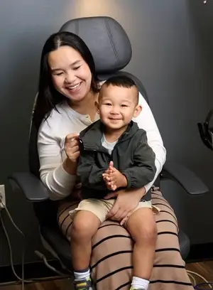 A woman sitting on a chair holding a child who is smiling and looking at something the woman is holding