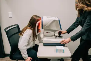 An optometrist uses an autorefractor on a patient at an eye clinic.