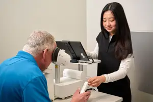 An older man is having an eye examination with a woman holding a machine in front of him.