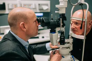 An older man is having an eye examination by a doctor with an ophthalmoscope
