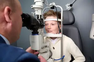 A man is examining a young boy's eyes with a microscope in a clinic.