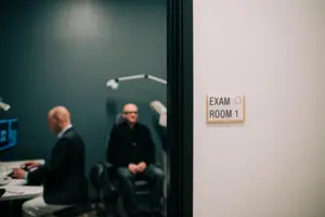 Two men sit in an exam room, one of them appears to be waiting for an appointment.