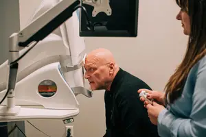 An elderly man with glasses is undergoing an eye checkup by a woman in a clinic.