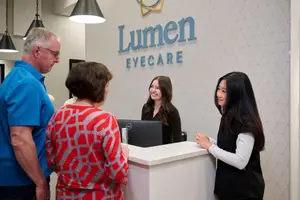 Four people in a Lumen Eyecare reception area smiling and talking to each other