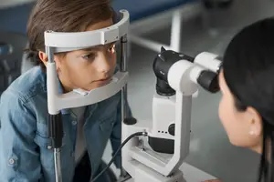 A woman is checking a boy's eyes with a microscope in an examination room
