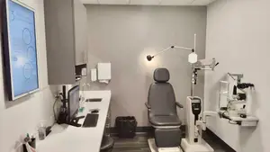 An exam room with an ophthalmoscope, a computer monitor, a desk, and a trash bin.