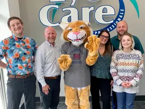 Six people posing with a tiger mascot in front of a sign for Eye Care Professionals