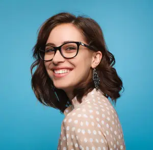 Portrait of a woman with brown hair and glasses smiling in front of a blue background