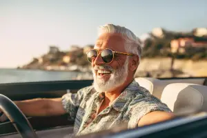 A man is sitting inside a convertible car and smiling while holding the steering wheel