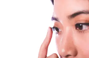 Close up of womans face wearing makeup and putting contact lens in her eye