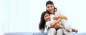 A smiling woman holding a young girl in her arms while sitting on a couch