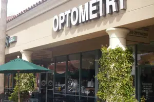 An optometry shop with a green umbrella in front of it.