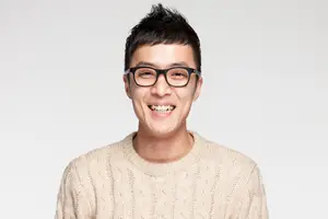 Man wearing glasses and a white sweater smiling for the camera