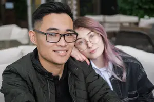 Man with glasses and woman with pink hair sitting on a couch in a restaurant