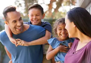 Three people, including a man, a boy, and a girl, are smiling and seem to be posing for a photo in an outdoor area, possibly in a garden.