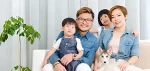 A family with two kids and a dog sitting on a couch with a plant in the corner of the room