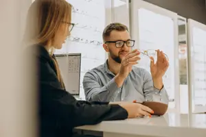 A man is holding a pair of glasses while a woman looks on in a shop.