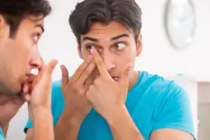 Man putting in a contact lens while looking in a mirror
