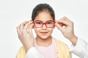 Young girl in red glasses being adjusted by a doctor