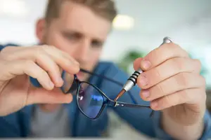 A man is adjusting a pair of glasses with a tool.