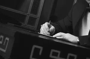 A man in a suit writing on a piece of paper with a pen