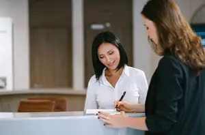 A woman signing a document at a reception desk with another woman