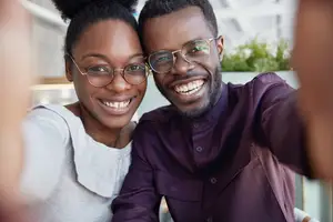 A couple smiling at the camera while wearing glasses