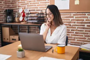 A woman sitting at a desk with a laptop and coffee mug, smiling and looking at the camera