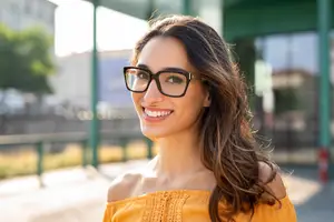 Portrait of a smiling woman with glasses standing outside.