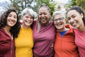 A group of women with different ages and backgrounds are standing and smiling in an outdoor area.