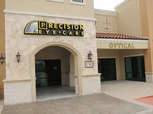 Exterior view of Precision Eye Care optical shop with glass doors and windows, a black arched entrance, and a yellow sign with the words 'Precision Eye Care' on a beige wall.