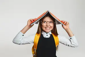 Girl holding a book over her head smiling and wearing glasses and a backpack