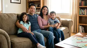 A family sits on a couch and smiles for the camera, a game of Monopoly is on the coffee table in front of them.
