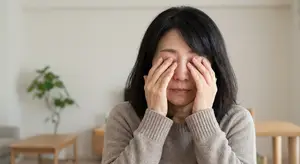 an older Asian woman sitting at a table with her hands covering her face