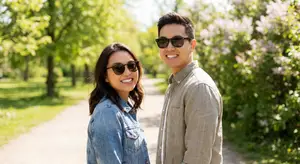 A man and woman wearing sunglasses pose for a picture in a park.