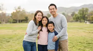 A family of four, a woman, a girl, a boy, and a man, standing together in a park.
