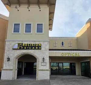 Front entrance of the Precision Eye Care Optical store building with a yellow sign and lamps