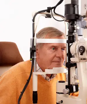 An older man is having his eyes examined by an eye doctor using a phoropter