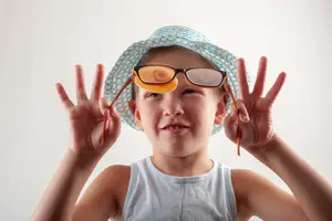 A young boy with a hat and glasses smiles and gives a peace sign with his hands