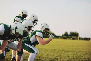 A group of football players in green and white uniforms playing football on a field with a grassy surface