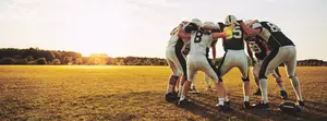 Football players in a huddle on a field with a sunset in the background