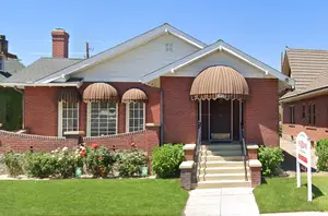 A red brick house with three windows and a door under a brown awning on a sunny day.