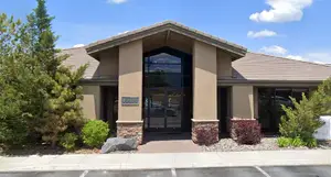 A building with a brown roof, glass doors, and plants outside on a sunny day.